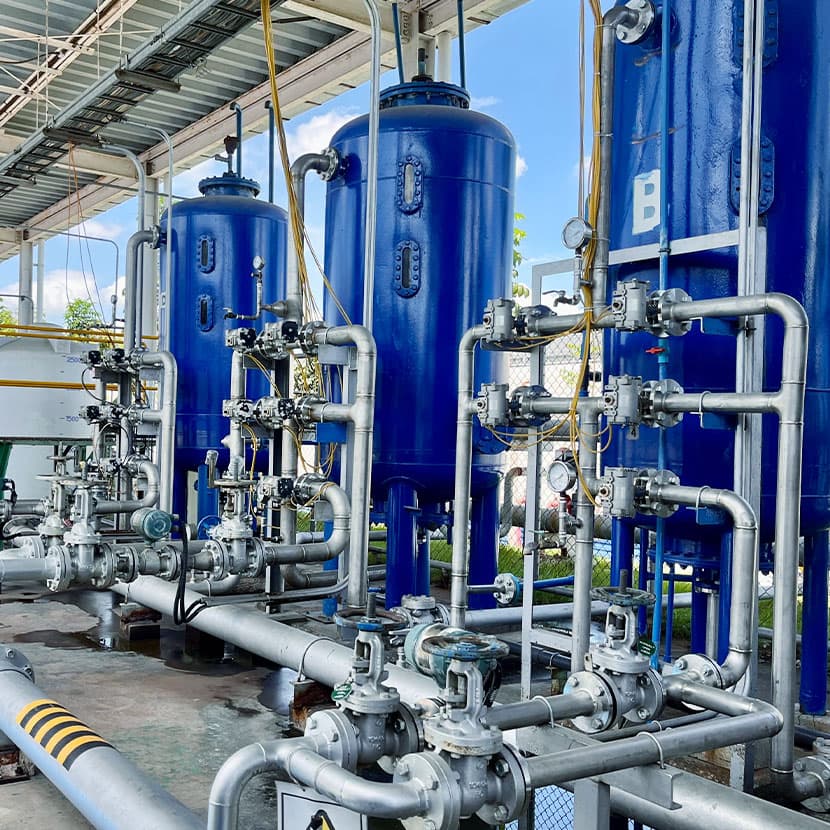 Industrial filtration and processing system with blue pressure vessels, stainless steel piping, valves, and gauges under a covered structure