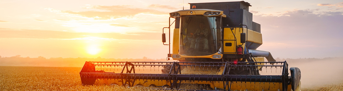 Picture-showing-a-grain-harvester-harvesting-wheat-against-a-cloudy-orange-sunset-sky.